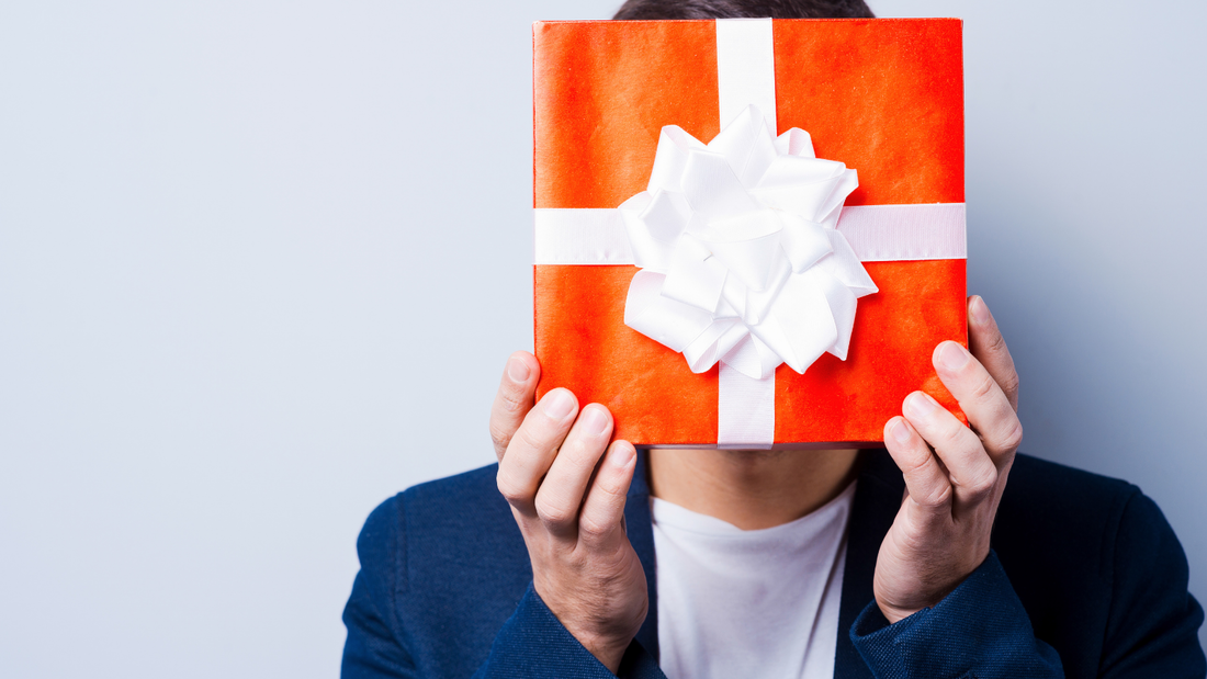 Picture of man holding orange Christmas gift in front of face