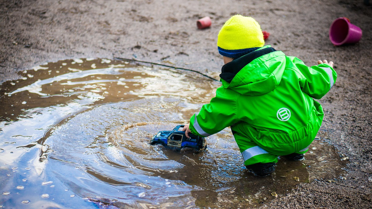 Picture of child in outdoor winter clothing playing in a big puddle.